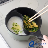 一個雙鍋，一邊是米粥，另一邊是炒蛋和蔥，用筷子將其攪拌