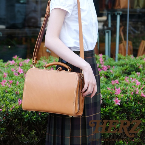 職人手作淺棕色皮革方形兩用單肩包，附有提把和可調式長背帶，採用拉鍊開合。