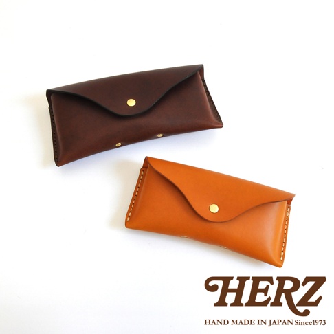 兩個職人手作皮革眼鏡收納盒，一個深棕色，一個淺棕色，皆有金色釦子，背景為白色。