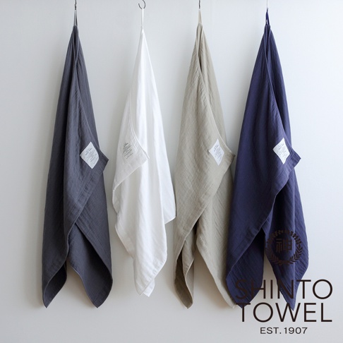 四條2.5層紗浴巾，分別為深灰色、白色、卡其色及海軍藍，皆為L尺寸，懸掛於牆面。