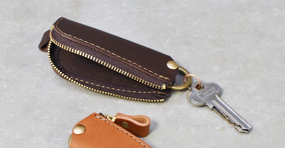職人手作咖啡色皮革Organ拉鍊鑰匙包，配有金色拉鍊、銅質铆釘及鑰匙圈，可收納鑰匙。另有一棕褐色皮革鑰匙包局部。