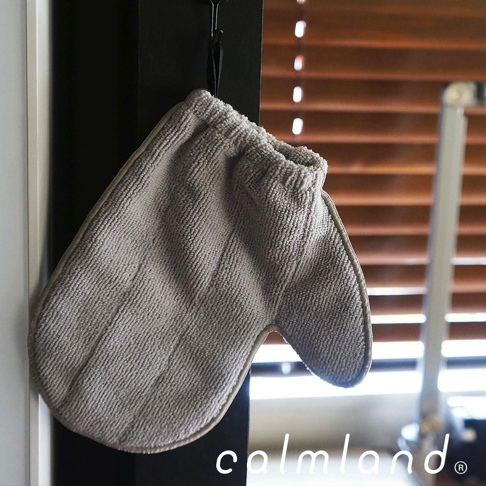 一隻淺灰色超細纖維除塵清潔手套，手套材質柔軟，表面有細緻紋理，掛在黑色掛鉤上，背景為木質百葉窗。