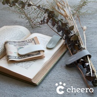 三款萬能QQ變形夾，分別為淺灰、淺綠和白色，皆為矽膠材質，印有「cheero」字樣，夾在裝有美鈔的書本和乾燥花束上。