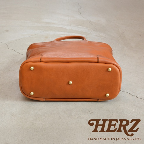 日本HERZ 職人手作皮革Organ兩用拉鍊托特包 G-45，俯視角度，展示包款底部黃銅腳釘及品牌標誌「HERZ HAND MADE IN JAPAN Since1973」。