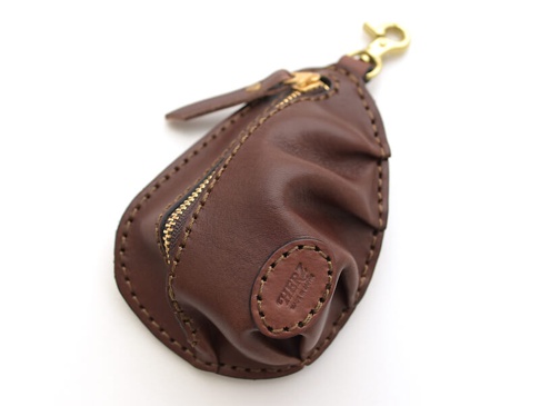職人手作咖啡色皮革餃子造型零錢包，帶有黃銅色拉鍊與掛鉤，皮革表面有細緻的壓紋和縫線。