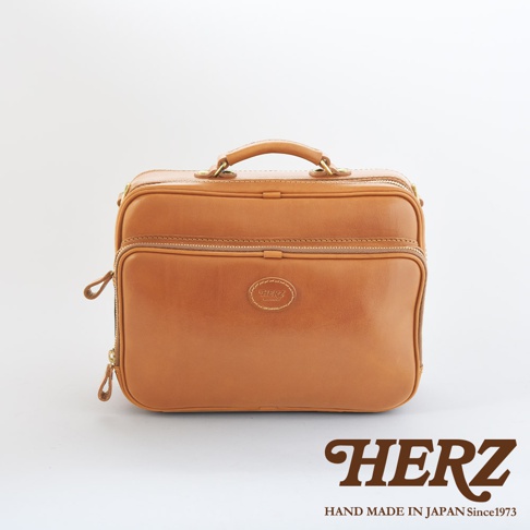 職人手作皮革兩用商務公事包，淺棕色牛皮材質，擁有雙拉鍊隔層、頂部提把及側邊拉鍊設計，正面中央有品牌橢圓形皮革標誌。