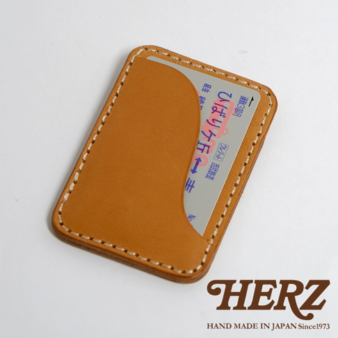 職人手作皮革名片收納夾，淺棕色皮革，縫線精緻，內插一張日文卡片，右下角有HERZ品牌標誌。