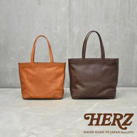 兩個職人手作皮革托特包，分別為橘棕色和深棕色，皆為立體方形設計，搭配簡潔的提把，底部有加固設計。