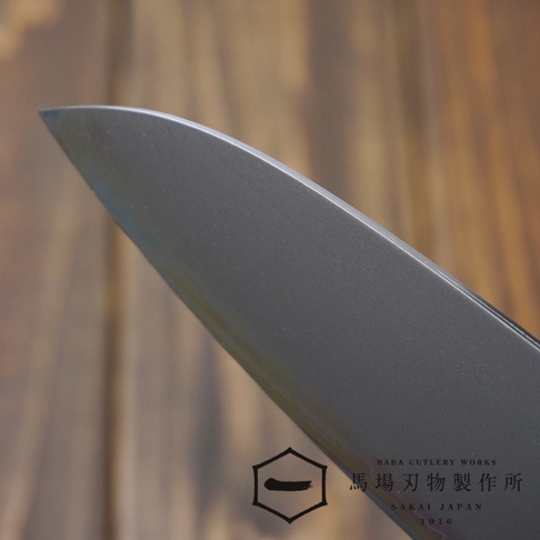 [景清] Chromax鋼三德刀，刀刃為銀灰色，表面光滑，刀尖鋒利，背景為淺棕色木紋。