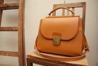 職人手作的淺棕色皮革兩用單肩包，帶有黃銅色鎖扣和縫線細節，整體風格簡約。