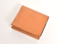 淺棕色皮革製成的職人手作直式卡片收納雙折短夾，表面光滑，帶有細緻的車縫線，右側有拉鍊設計，皮革紋理自然。