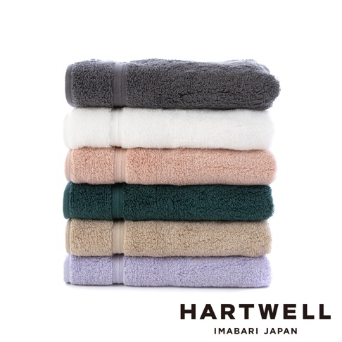 一疊六條今治毛巾，顏色由上至下分別為：炭灰色、白色、淡粉色、深綠色、淺褐色、淺紫色。毛巾皆為純色，質地柔軟，邊緣有細緻的織帶裝飾。