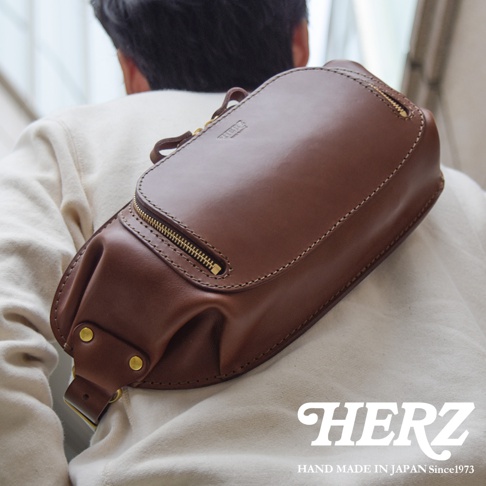 HERZ 職人手作皮革拉鍊旅行斜背包，駝色皮革材質，以斜背方式展示於模特兒背上，強調日本製造。