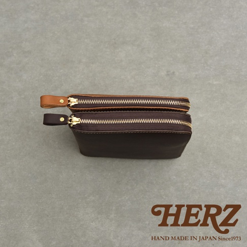 兩款職人手作皮革記事本收納包，一個為棕褐色，另一個為深咖啡色，皆配有金色拉鍊和皮革拉環。