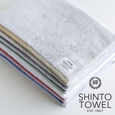 YUKINE 雪中漫步系列有機棉蓬厚浴墊，層疊展示多種柔和色系，包括淺灰、米黃、淺綠、紅色、藍色等。浴墊材質蓬鬆柔軟，邊緣車縫整齊，頂部可見白色標籤，印有品牌名稱及日文。