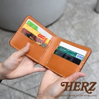 職人手作的棕色皮革二折橫式小短夾，內含多個卡槽，展示有信用卡、會員卡及紙鈔。