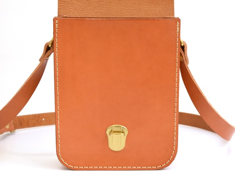 淺棕色皮革製作的單肩包，有翻蓋設計，搭配金色金屬扣，整體以縫線裝飾。
