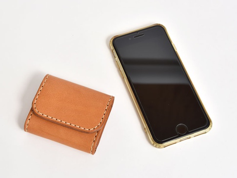 焦糖色皮革雙折收納零錢包，縫線清晰，旁邊為金色邊框的黑色手機。