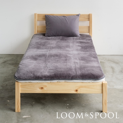 單人床鋪上鋪有灰色美麗諾羊毛厚感保暖墊，墊子上方擺放一個灰色枕頭，床架為淺色木質。