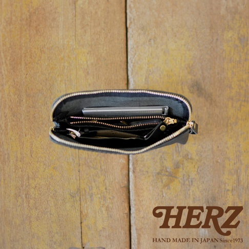 職人手作黑色皮革Organ雙拉鍊收納袋，內部展示有手機、鑰匙、零錢包等物品，拉鍊為金色，整體置於木紋背景上。