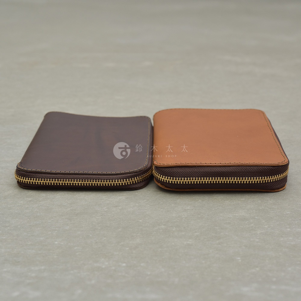 兩個皮革記事本收納包，一個深棕色，一個淺棕色，皆有黃銅色拉鍊，擺放在灰色背景上