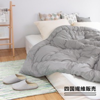 灰色棉被蓋在床上，旁邊有兩雙條紋拖鞋，床頭有幾個抱枕。