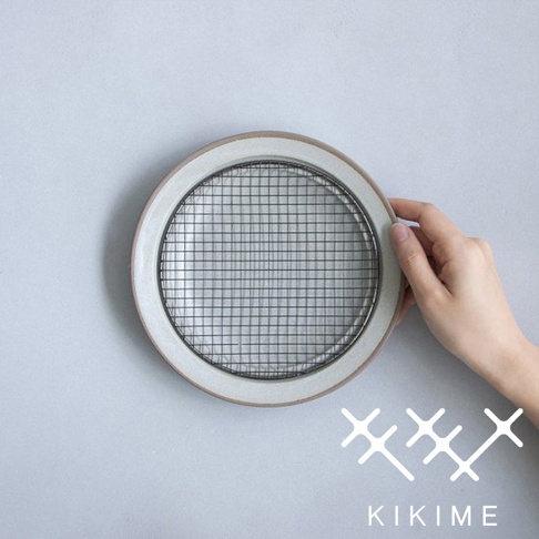 美濃燒瀝油餐盤，圓形陶瓷盤身帶有淺灰邊緣，內嵌黑色金屬網架，由手部持握展示。