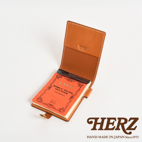 職人手作淺棕色皮革便利貼收納套，附帶一本橘色封面、印有「LIFE NOBLE MEMO SECTION」字樣的筆記本，收納套內有品牌壓印，可固定筆記本。