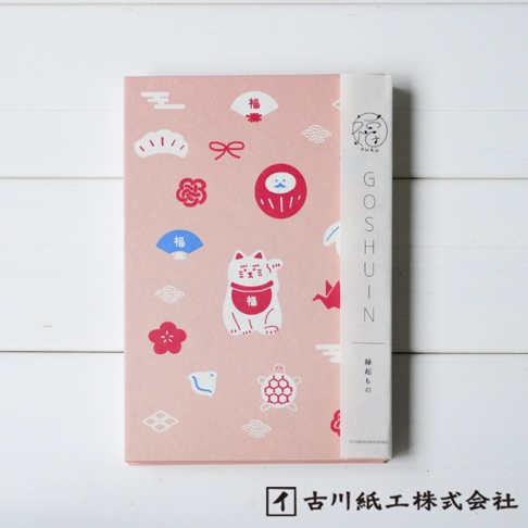 粉紅色和紙御朱印帳，印有白色招財貓、紅色達摩、藍色與紅色日式扇子、紅色花朵、白色烏龜、紅色紙鶴等多種可愛吉祥物圖案。