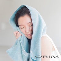 一位女性頭部包覆著淺藍色、柔軟的毛巾，毛巾材質蓬鬆，有鈕扣設計，品牌 Logo「ORIM」標示於右下方。