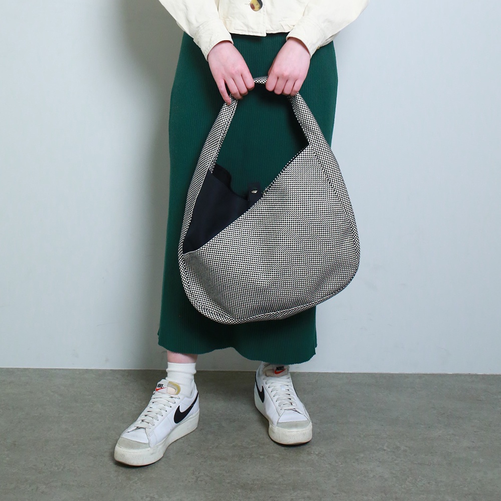 一名女性手提著一個三河木綿刺子織半月包，包身為黑白細小棋盤格紋，內部露出黑色內袋。