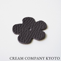 深棕色皮革製成的四葉草形狀飾品，表面有壓紋，中心有一個小圓孔。