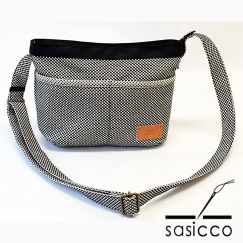 三河木綿刺子織肩背包，黑白格紋布料，附有可調整背帶與皮革標籤。