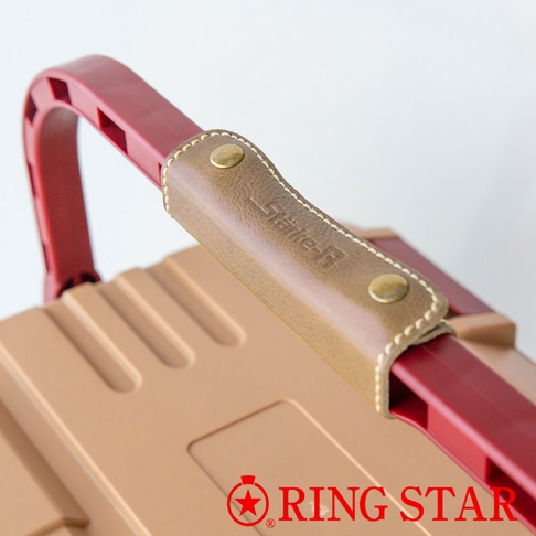 Starke-R 超級箱特寫，展示了紅色的提把，上方覆蓋著一個咖啡色皮革製成的提把套，以白色縫線裝飾，並有兩顆黃銅色铆釘固定。箱體主體為淺棕色，表面有凹槽設計。