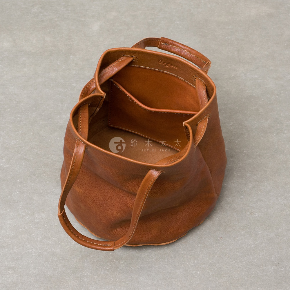 這款日本HERZ旗下Organ系列的棕色皮革手提托特包，呈現簡約圓桶外型，頂部設有抽繩設計，內側配有一個貼式口袋並印有Organ字樣，底部則有SUZUKI SHOP的商標浮雕，由上方俯視視角拍攝，展現細膩的手作皮革質感。