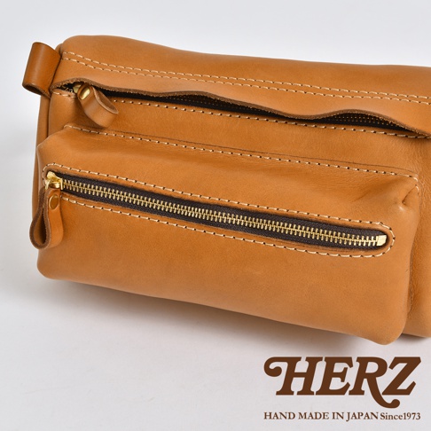 職人手作皮革腰掛斜背包，採用淺棕色皮革，帶有明顯的縫線和黃銅色拉鍊，設計簡潔實用。