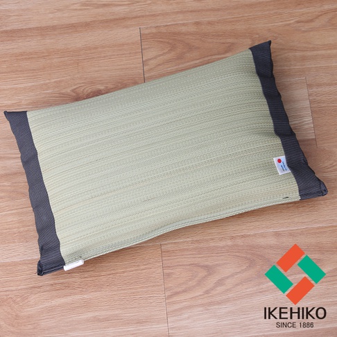 淺綠色藺草編織的長方形枕頭，兩側有深藍色條紋滾邊。枕頭表面有細緻的編織紋理，右側有一個標示「Made in Japan」的小白標籤。