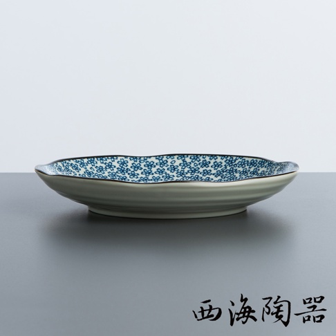 日本美濃燒陶瓷圓盤，盤面印有藍色小花圖案，盤緣帶有波浪紋路，盤身為米白色。