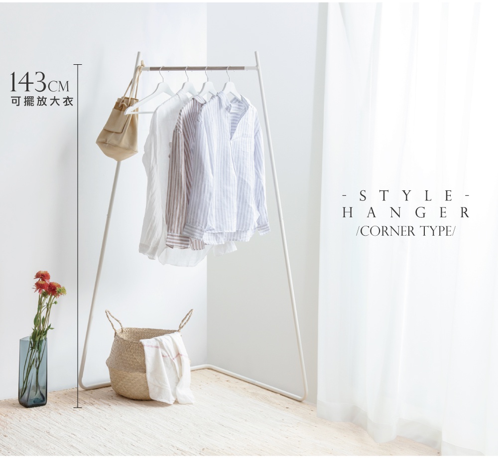 白色金屬角落造型吊掛衣桿，掛有數件條紋及素色襯衫，一側掛著卡其色帆布包，下方擺放草編籃與花瓶。