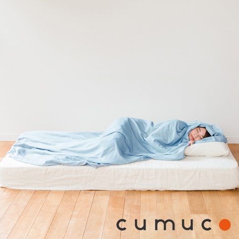 一位女子仰躺在床墊上，蓋著一條淺藍色的四層紗輕暖舒柔四季毯，毯子質地輕柔，邊緣垂墜。