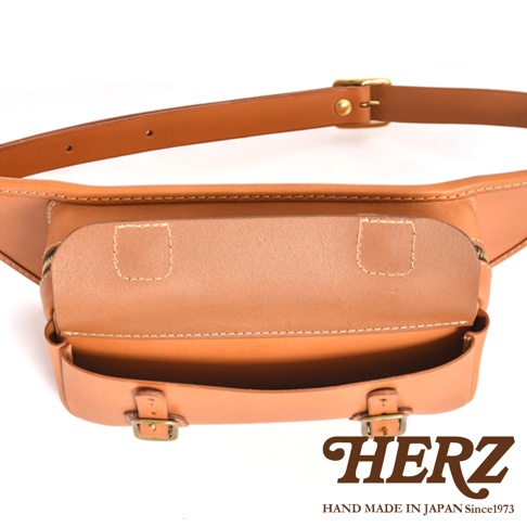 職人手作皮革騎士隨身斜背包，以天然皮革製成，呈現溫潤的淺棕色，設計簡潔實用，可調整式皮帶搭配黃銅扣環，展現經典風格。