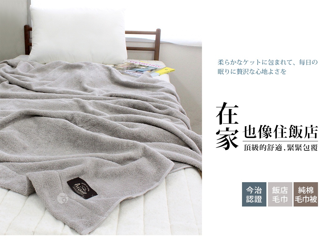 灰色今治飯店毛巾被，材質柔軟，蓋在床上，一角有黑色標籤，標示品牌與產地。