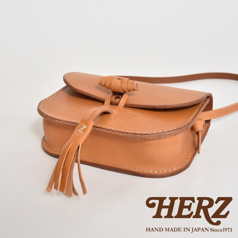 職人手作皮革流蘇側背包，淺棕色，天然皮革材質，帶有旋轉式皮革鈕扣開合及懸掛式皮革流蘇裝飾。
