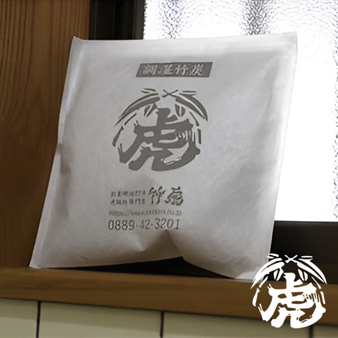 白色紙袋裝有調濕孟宗竹炭，袋上印有灰色「虎」字圖案、日文說明及電話號碼。