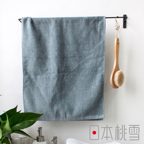 一條藍灰色、觸感細膩的今治柔絨浴巾，懸掛於黑色毛巾架上，旁邊掛著一支木柄沐浴刷。