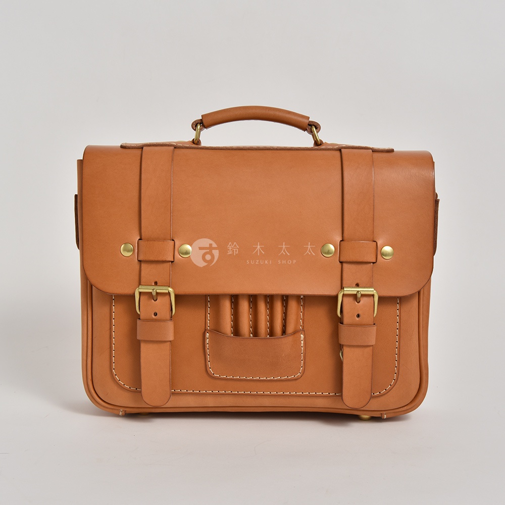 職人手作皮革傳統歐風三用學生包，呈現經典棕褐色，以高品質皮革製成，搭配黃銅色金屬扣環與鉚釘，包款正面有精緻縫線裝飾及一條皮革提把。