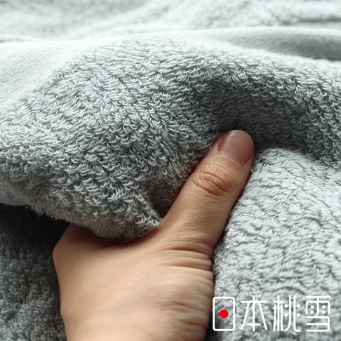 一隻手正輕柔地按壓著淺灰色今治匹馬棉方巾，展示其柔軟的織紋與蓬鬆的觸感。