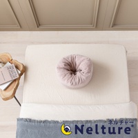 粉紅色毛巾材質的甜甜圈枕，置於米白色床單上，旁邊有一個木製邊桌，上面放著兩本雜誌。