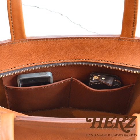 這款皮革托特包內有兩個隔層，一個隔層裡放著手機，另一個隔層裡放著一個小零錢包。