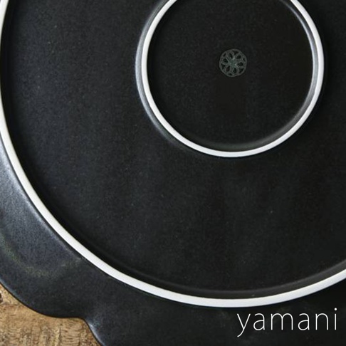 Tsudoi 黑鐵釉美濃燒花型盤，盤面為深黑色，帶有細微紋理，邊緣有立體花型，盤底有白色細邊，中央印有綠色花紋圖案。